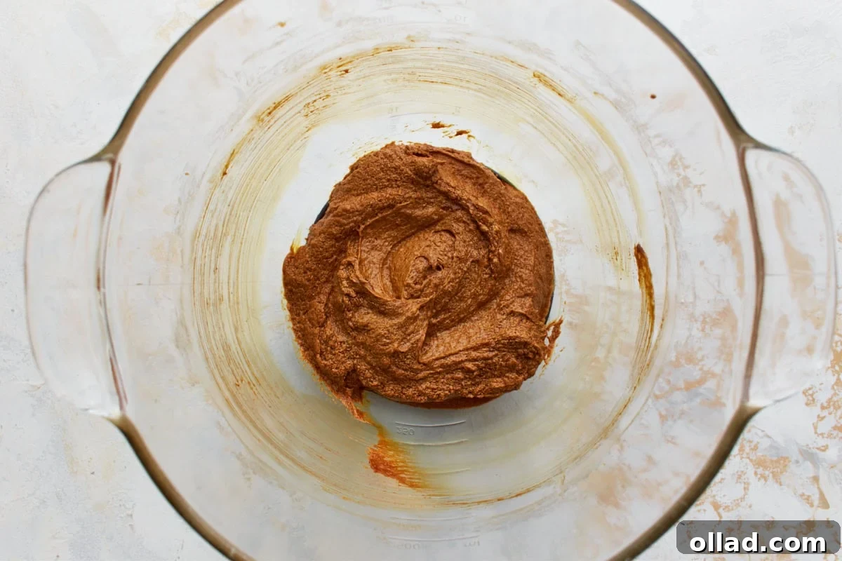 Gluten Free Gingerbread Delights 8 A single large egg, dark molasses, and pure vanilla extract have been added to the fluffy butter and sugar mixture in a glass mixing bowl, awaiting blending for gluten-free gingerbread cookies.