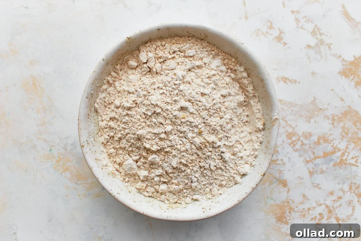 Gluten Free Gingerbread Delights 9 A medium-sized mixing bowl filled with the dry ingredients for gluten-free gingerbread cookies: gluten-free flour, baking soda, salt, ground ginger, cinnamon, nutmeg, and allspice, ready to be whisked together.