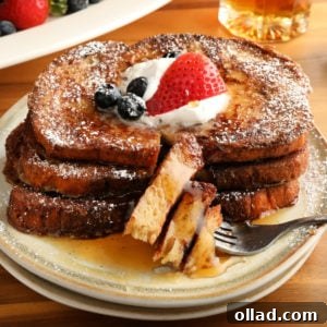 A top-down view of a square dish of Gluten-Free French Toast, richly browned, topped with fresh berries, a swirl of whipped cream, and a generous pour of maple syrup, all presented on a crisp white plate beside a fork.