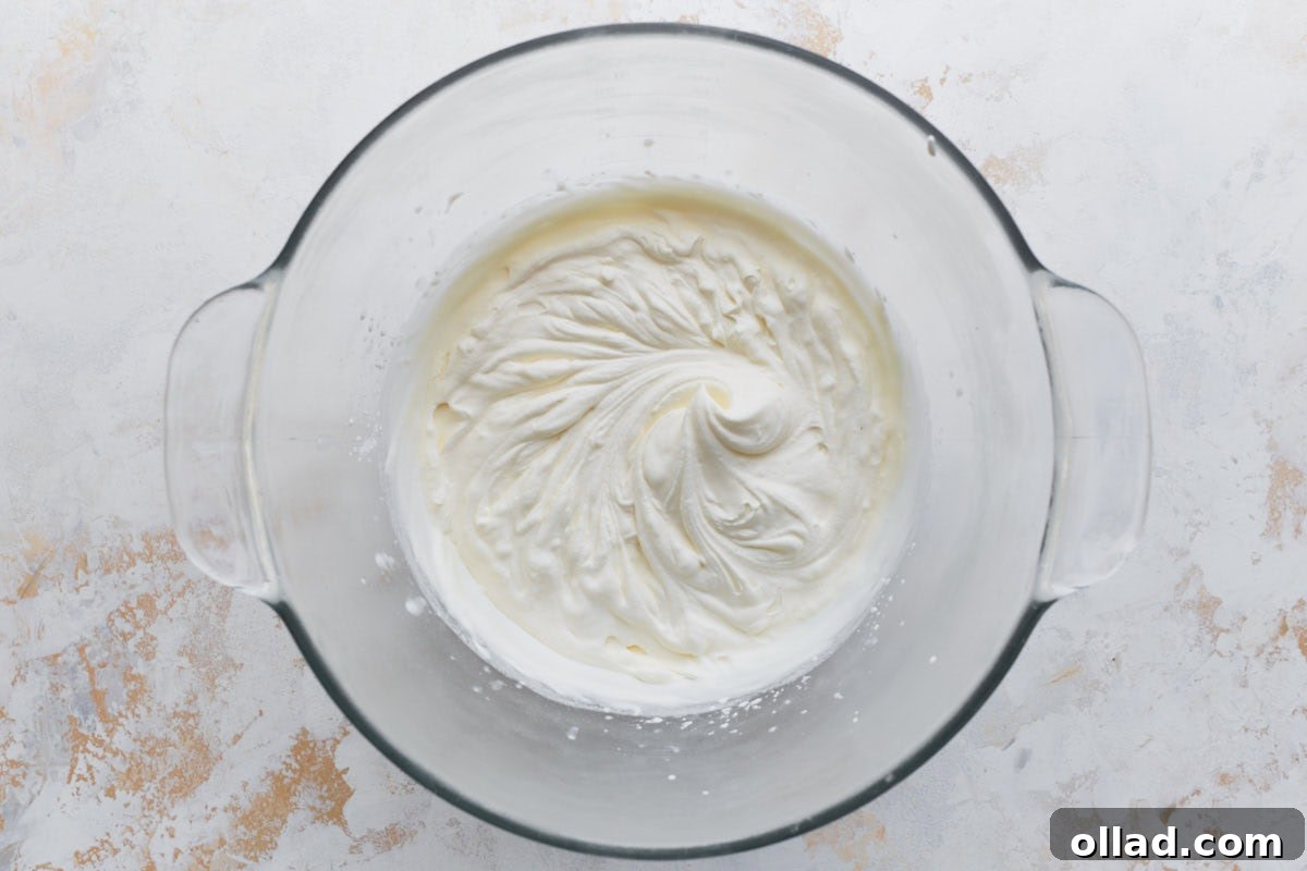 Decadent Gluten-Free Ice Cream Cake 15 A glass mixing bowl with freshly whipped cream, showing soft, glossy peaks after mixing with vanilla, powdered sugar, and cornstarch.