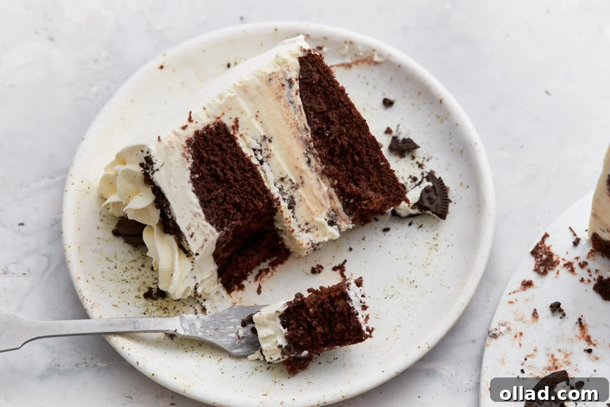 Decadent Gluten-Free Ice Cream Cake 23 A single slice of gluten-free ice cream cake on a plate, with visible layers of chocolate cake, cookies and cream ice cream, and whipped cream frosting, partially eaten with a fork.