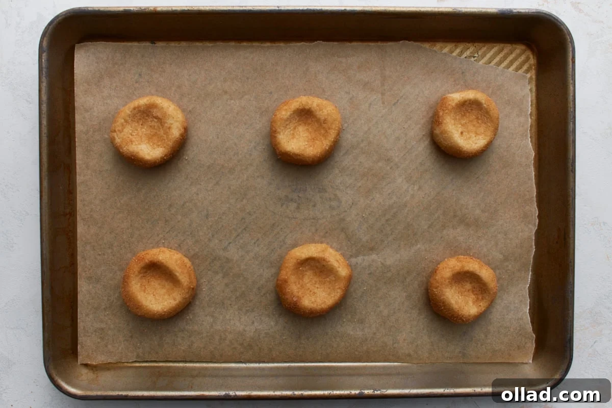 Chewy Gluten-Free Snickerdoodle Delights 11 A parchment-lined baking sheet displays six meticulously placed, coated cookie dough balls, each slightly pressed in the center, demonstrating proper preparation before baking the gluten-free snickerdoodles.