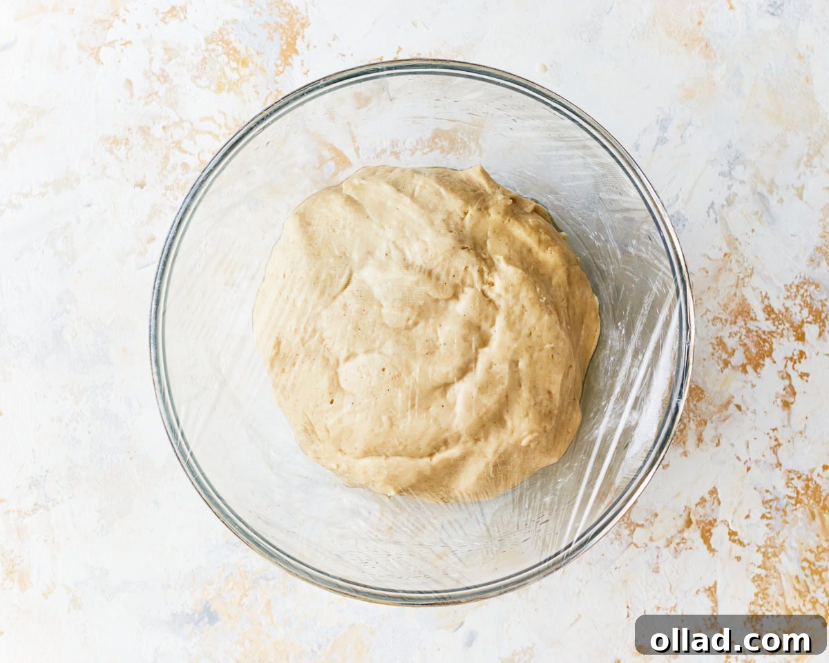 Irresistible Gluten-Free Cinnamon Rolls 10 a risen ball of dough in a glass bowl covered with plastic wrap.