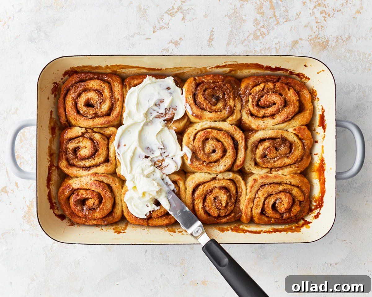 Irresistible Gluten-Free Cinnamon Rolls 21 spreading frosting over gluten-free cinnamon rolls with an offset spatula.