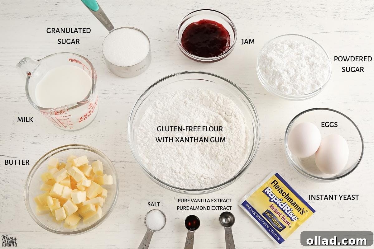 All the ingredients for gluten-free Danish pastries laid out neatly on a white counter, including flour, sugar, butter, milk, eggs, vanilla, almond extract, salt, and raspberry jam.
