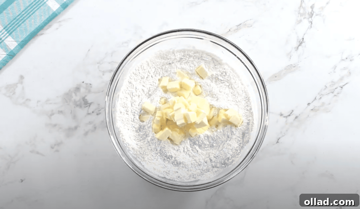 Cubes of softened butter are added to the flour mixture in a glass mixing bowl, ready to be cut in using a pastry cutter