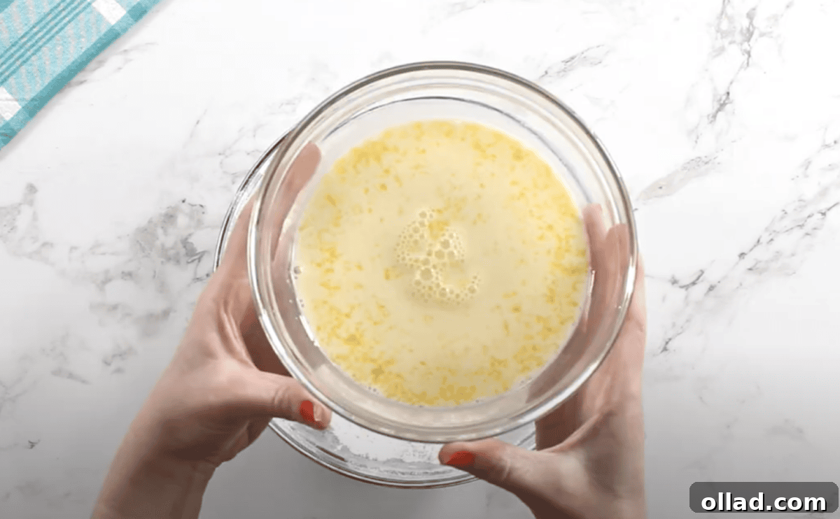 A glass bowl filled with a whisked mixture of milk, egg yolks, vanilla, almond extract, and salt, held over the flour mixture.