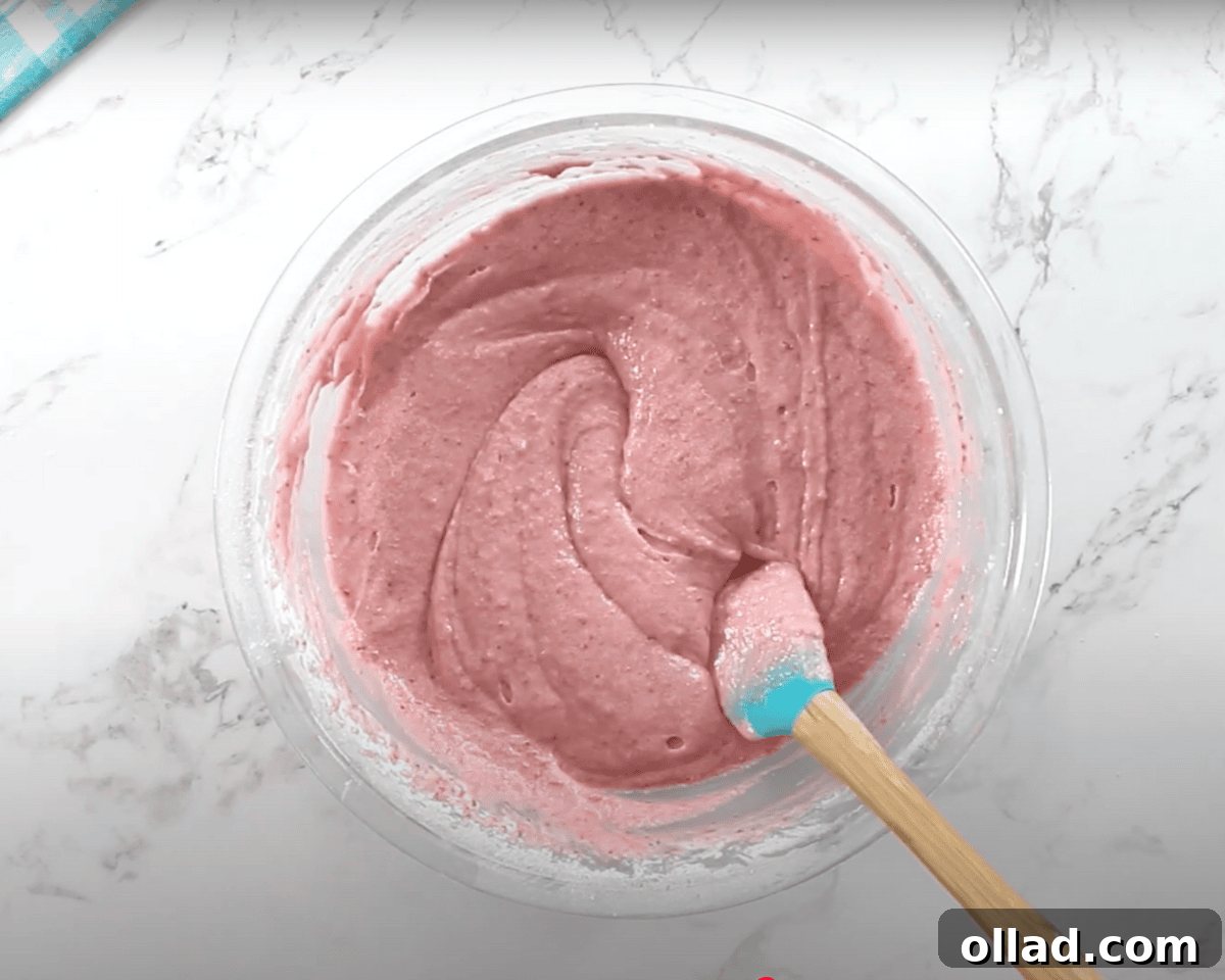 A fully mixed gluten-free strawberry cake batter with a pinkish hue is being stirred with a silicone spatula.
