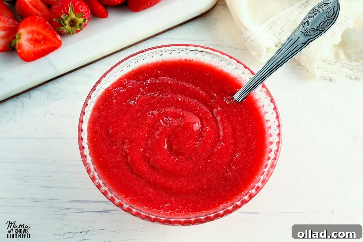Homemade strawberry reduction sauce in a clear glass bowl with a spoon, surrounded by fresh strawberries