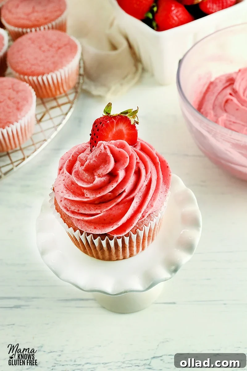 Strawberry frosting beautifully piped onto a strawberry cupcake, with a bowl of frosting, fresh strawberries, and more cupcakes in the background