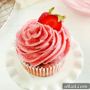 strawberry frosting piped on a strawberry cupcake topped with a sliced strawberry