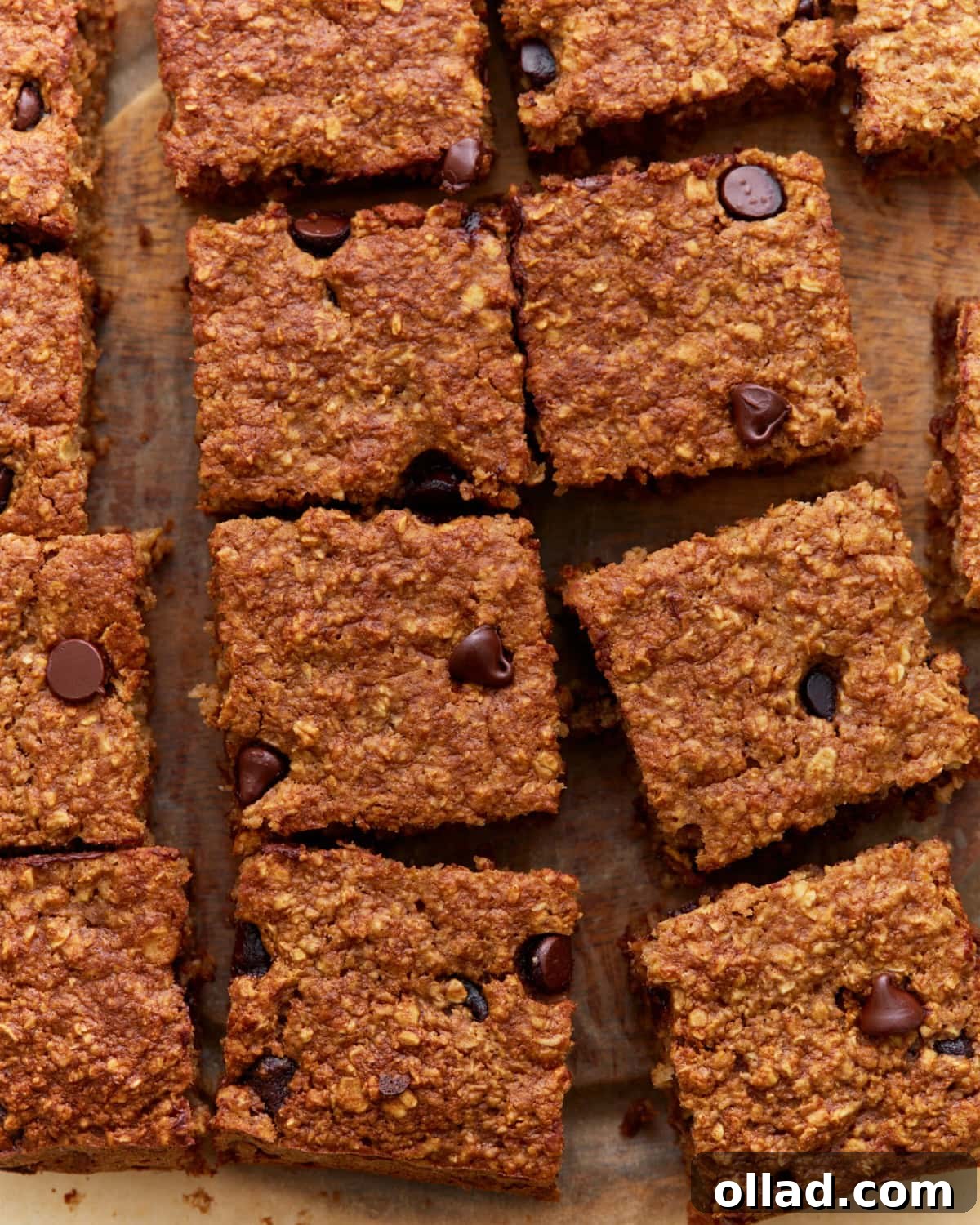 Close-up of sliced baked oatmeal bars with chocolate chips on a wooden surface, showing a golden-brown, chewy texture.