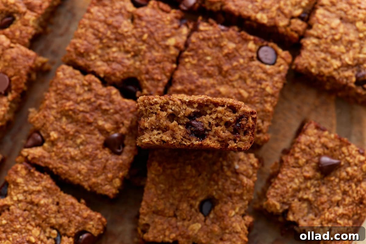 Close-up of a single oatmeal bar held above others, showing a moist, chewy interior with visible chocolate chips.