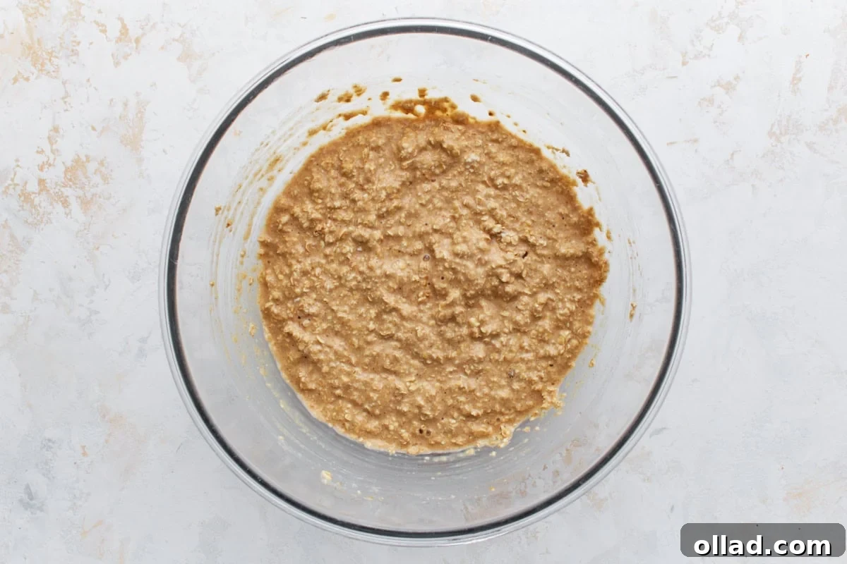 Wet and dry ingredients combined into a thick, textured oatmeal batter in a glass mixing bowl.
