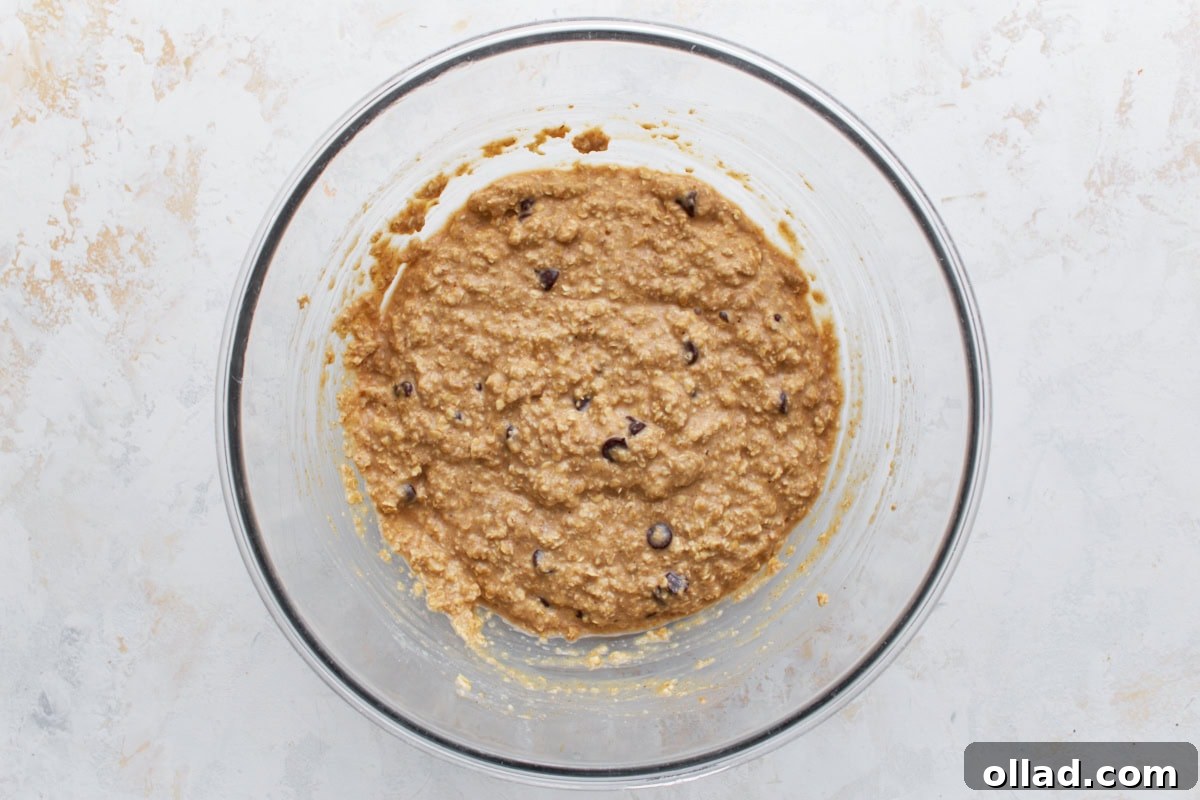 Oatmeal bar batter with chocolate chips stirred in, shown in a large glass bowl.