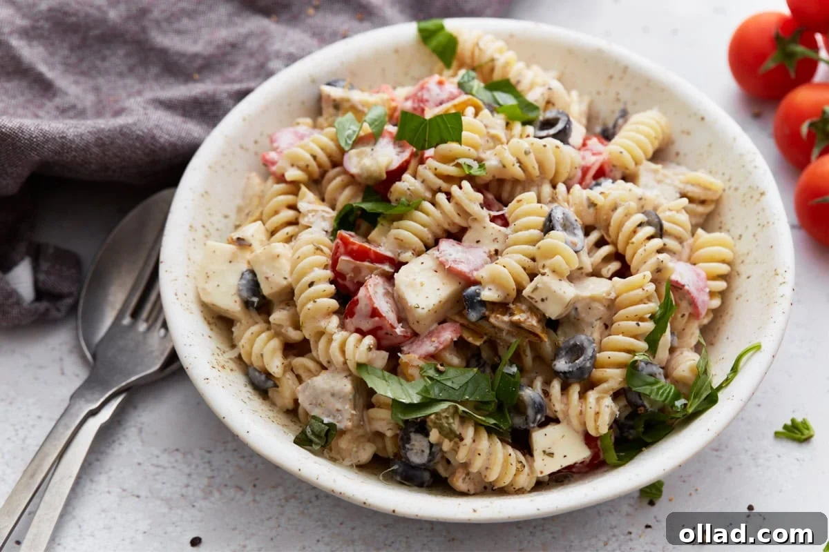 A tempting side view of a bowl of creamy Italian pasta salad, perfectly composed with a fork and spoon resting nearby, highlighting the vibrant colors and appealing textures of the various ingredients.