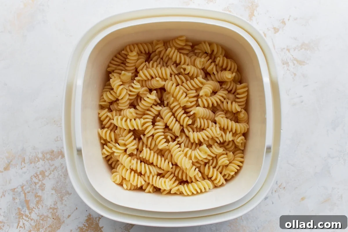 A close-up view of plain, perfectly cooked gluten-free rotini pasta resting in a white plastic colander, ready to be combined with other fresh ingredients for the pasta salad.