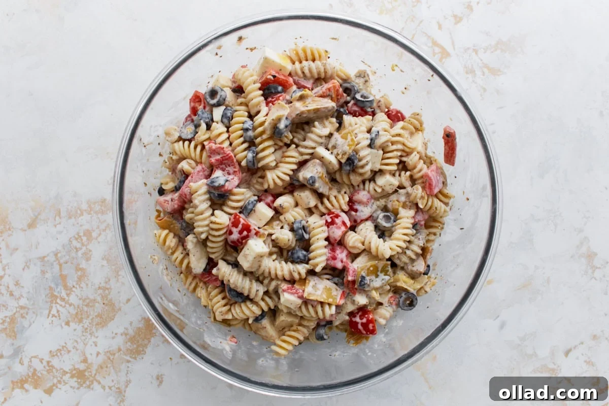 A large mixing bowl showcasing all the colorful pasta salad ingredients, now fully combined and glistening with the rich, creamy homemade dressing, demonstrating a well-coated and cohesive mix.