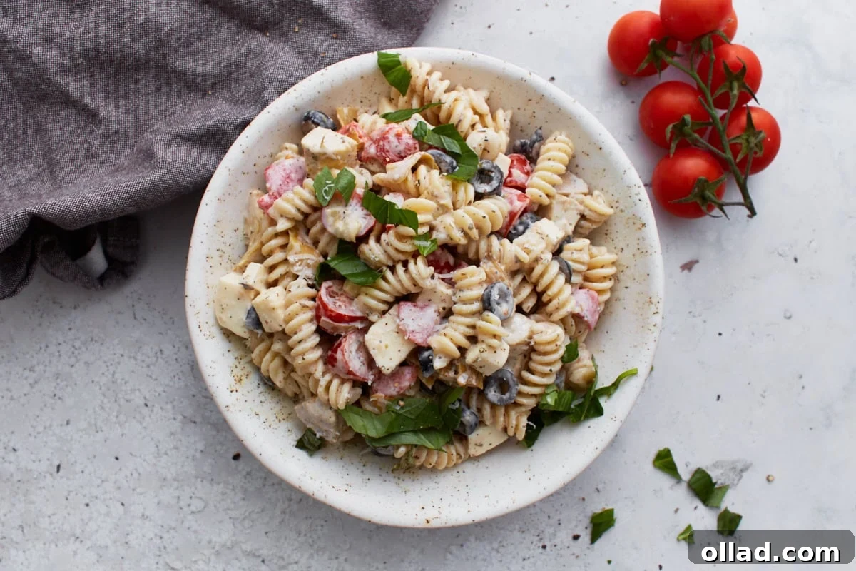 A delightful top-down perspective of a beautifully arranged bowl of creamy Italian pasta salad, artfully placed beside a cluster of fresh tomatoes on the vine and a folded linen napkin, ready for serving.
