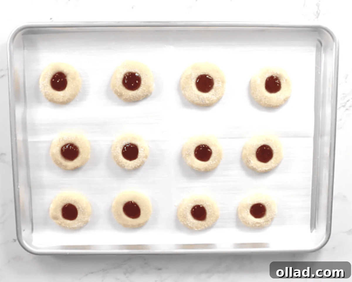 Gluten-free thumbprint cookies on a cookie sheet with jam filled centers, ready to go into the oven.