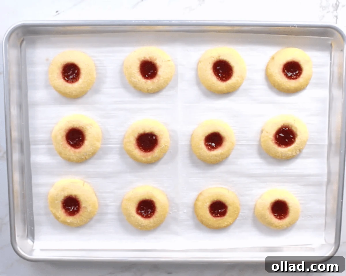 Gluten-free thumbprint cookies baking on a cookie sheet in the oven.