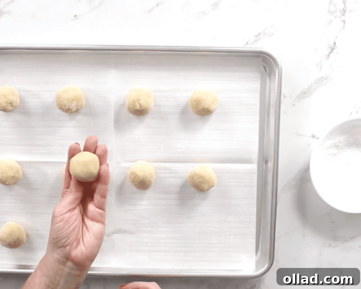 Rolling gluten-free thumbprint cookie dough balls on a baking sheet.