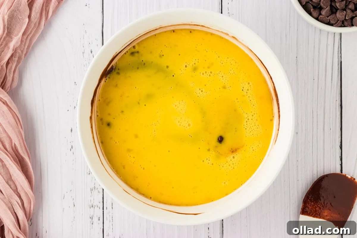 Whisked large eggs gently poured over the rich chocolate and sugar mixture in a white bowl, poised for incorporation.