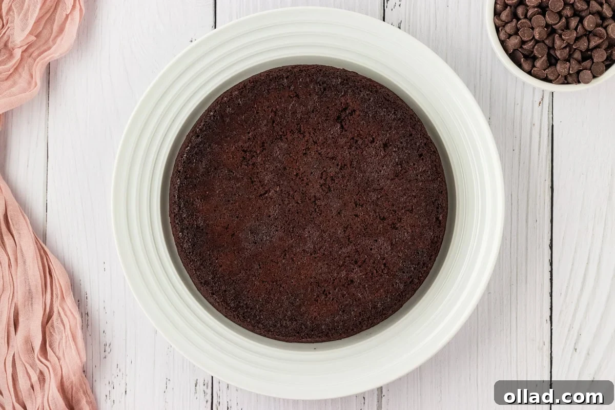 An inverted, fully cooled flourless chocolate cake resting on a pristine white cake plate, ready for its luscious ganache topping.