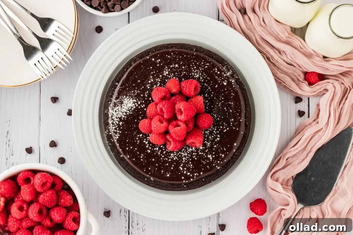 A stunning flourless chocolate cake, elegantly presented on a white platter, generously dusted with powdered sugar and adorned with fresh, vibrant raspberries, ready to be enjoyed.