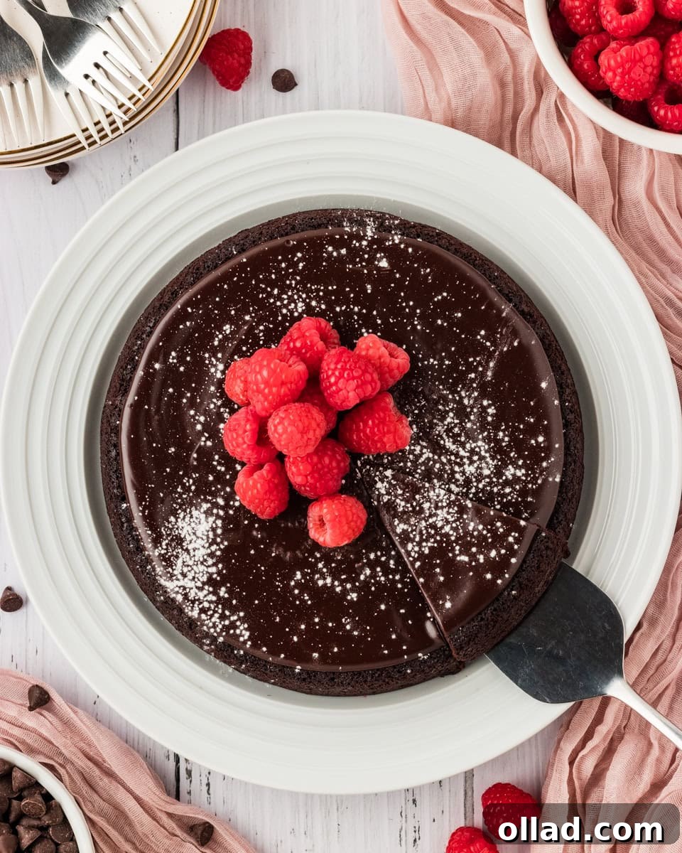 A metal cake knife carefully lifting a perfectly sliced piece of rich flourless chocolate cake from a larger cake, adorned with powdered sugar and fresh raspberries, presented on a pristine white plate.
