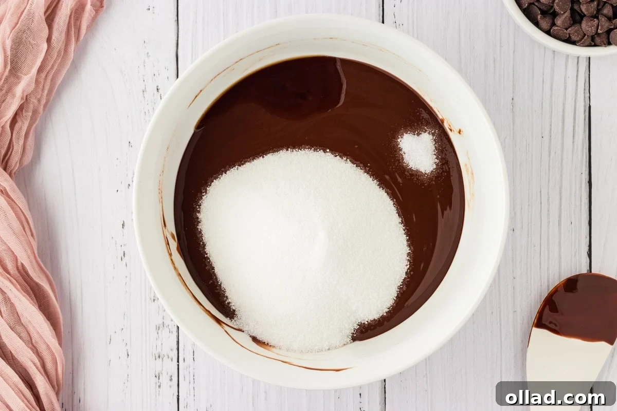 A bowl of melted chocolate and butter, with granulated sugar, salt, and pure vanilla extract added on top, ready for mixing.
