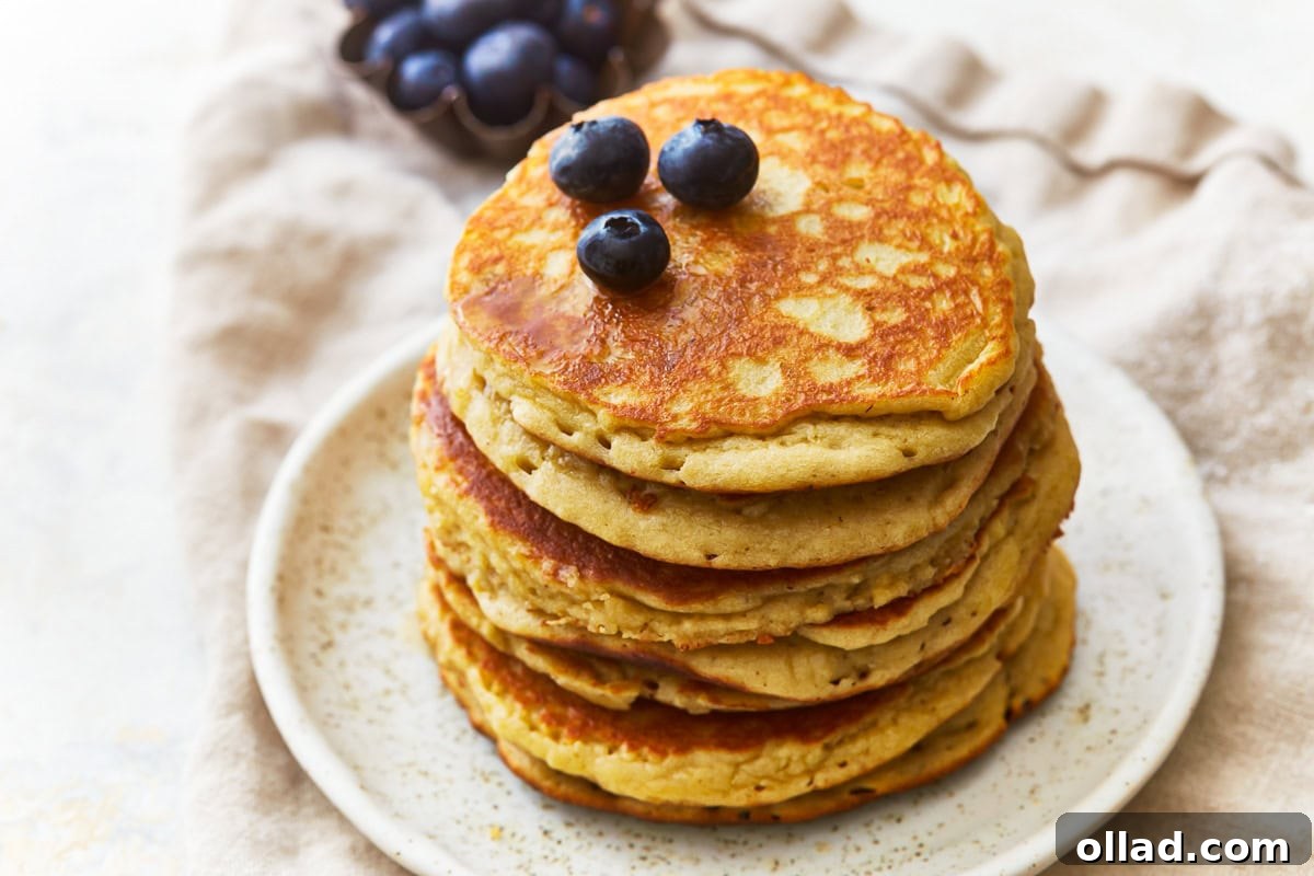 A close-up shot of a stack of fluffy almond flour pancakes, glistening with maple syrup and sprinkled with fresh blueberries, showcasing their inviting texture.
