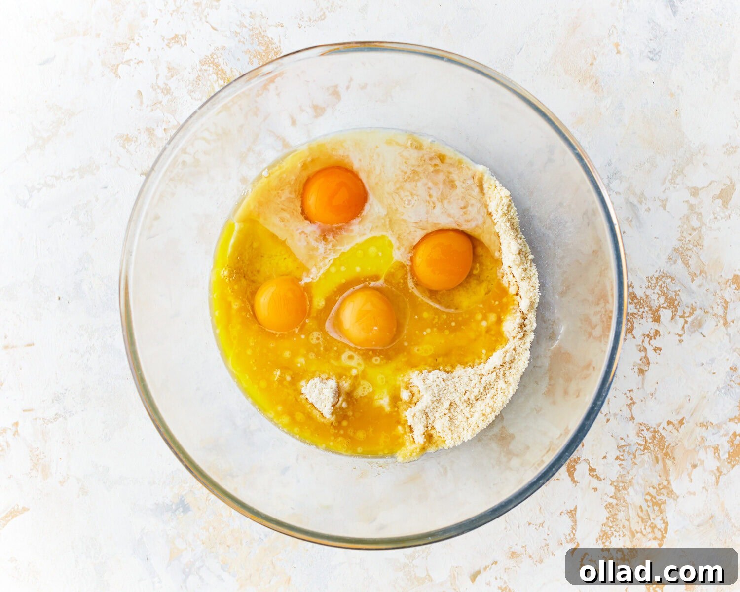 Wet ingredients, including eggs and cooled melted butter, being added to the dry mixture for almond flour pancakes in a large glass bowl.