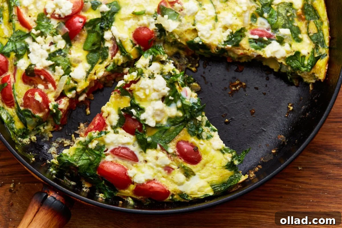 A perfectly baked slice of vegetable frittata, showcasing spinach, tomatoes, and crumbled feta, has been neatly removed from a cast-iron skillet, ready to be served.