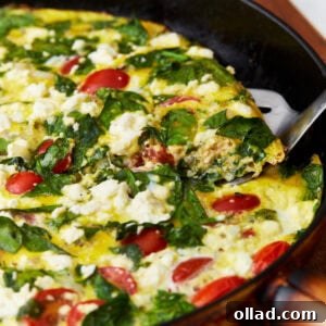 A smaller image showing a slice of frittata with tomatoes, spinach, and feta cheese being lifted out of a black skillet.