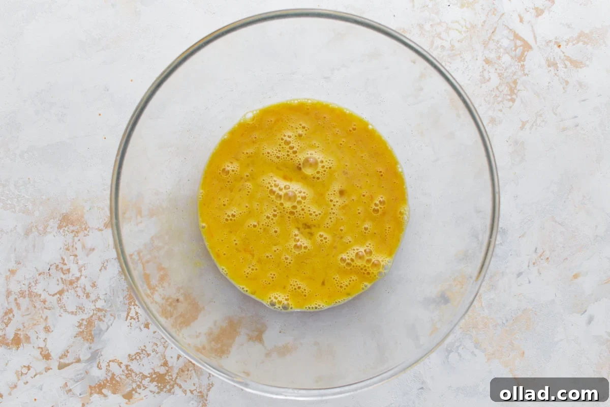 Freshly whisked eggs in a clear glass bowl, positioned on a bright, minimalist surface, ready for the next step in the frittata preparation.