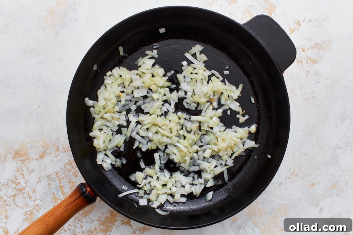 Diced yellow onions, now soft and translucent, gently sautéing in a black cast-iron skillet with a wooden handle, creating a flavorful base for the frittata.