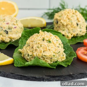 Close-up of vegan chickpea 'tuna' salad scoops served on fresh lettuce leaves, garnished with dill, lemon wedges, and tomato slices on a black slate platter.