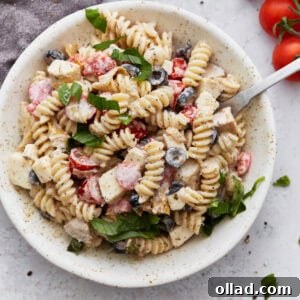 A bowl of creamy Italian pasta salad topped with fresh basil, filled with rotini pasta, cherry tomatoes, black olives, mozzarella cubes, and creamy dressing.