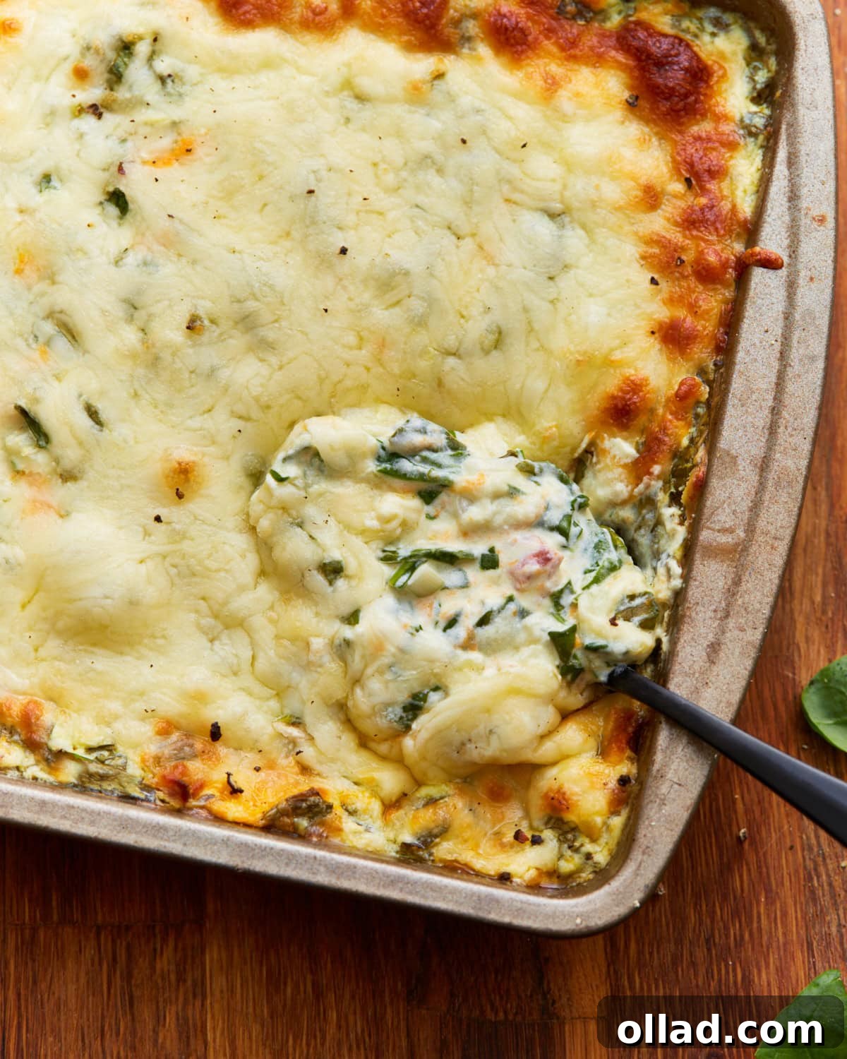 Spoon dipped into hot spinach dip in a tin baking dish on a wooden surface
