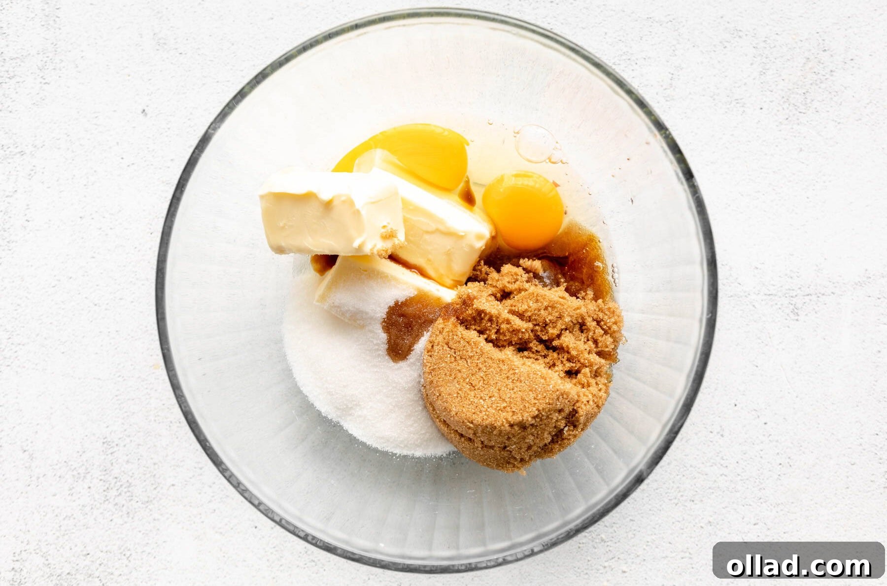 Softened butter, white granulated sugar, light brown sugar, and eggs in a separate glass bowl, ready for creaming.