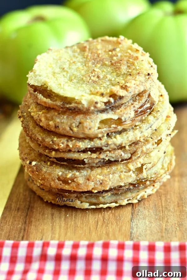 A stack of four perfectly golden gluten-free fried green tomatoes, with fresh green tomatoes blurred in the background, hinting at their raw beauty.