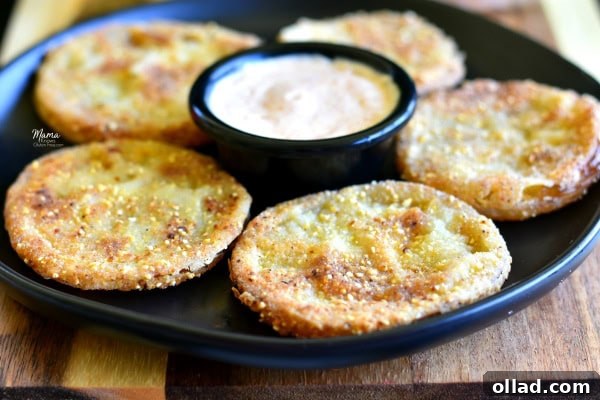 Five beautifully fried gluten-free green tomatoes arranged on a sleek black plate, accompanied by a small bowl of zesty remoulade sauce, ready to be enjoyed.