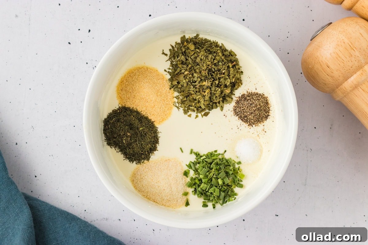 Overhead view of a bowl filled with dairy-free ranch base topped with piles of dried herbs and spices, ready to be mixed.