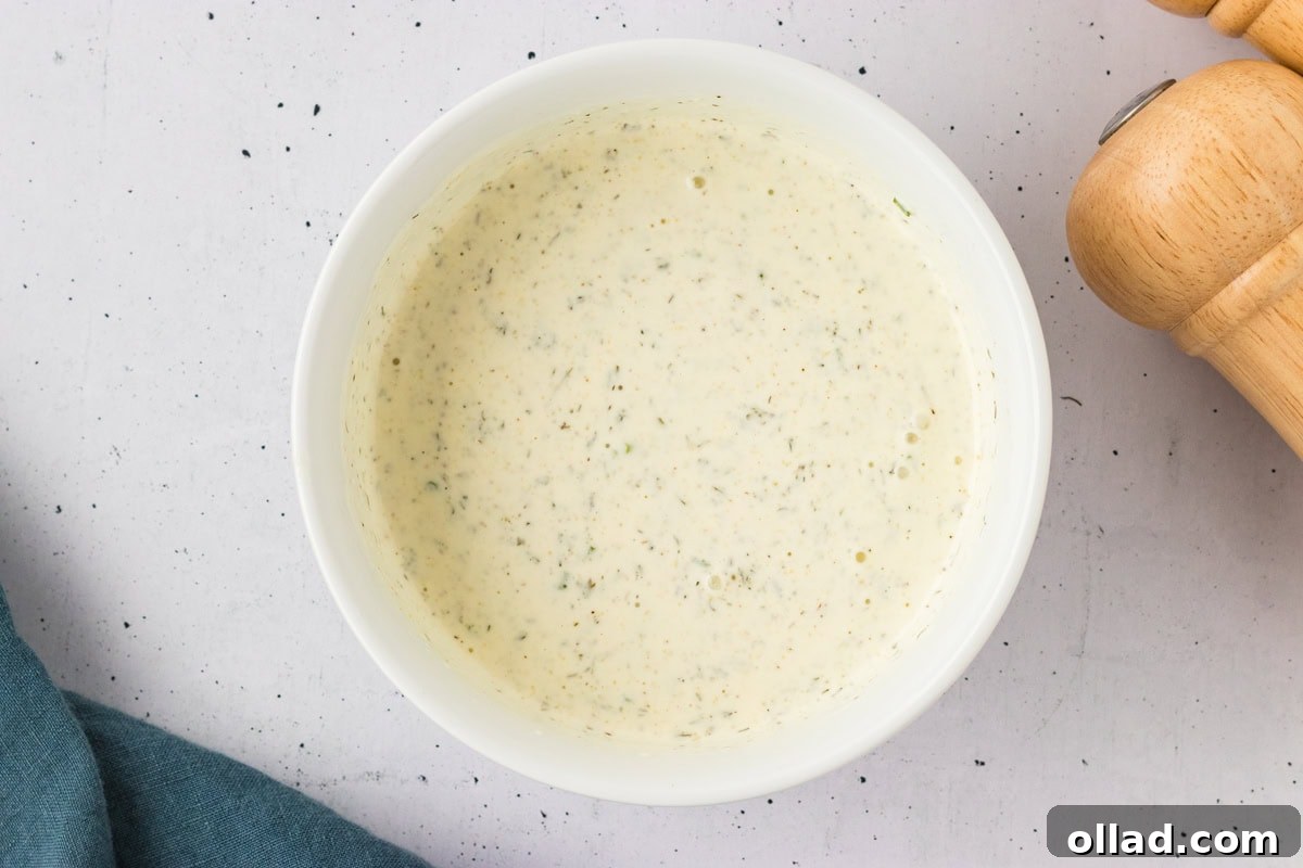Creamy dairy-free ranch dressing fully mixed in a white bowl, flecked with herbs and spices throughout.