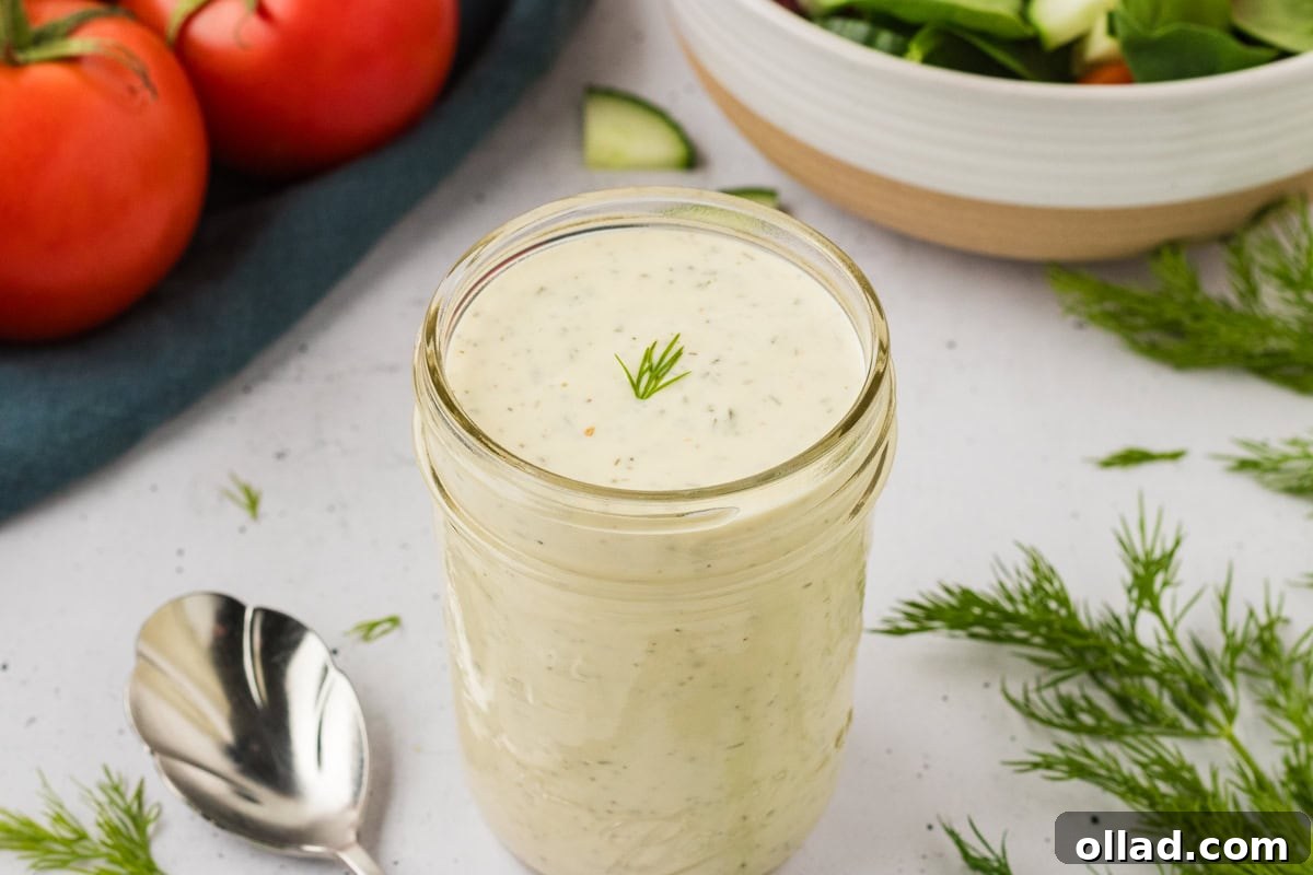 Close-up of a mason jar filled with dairy-free ranch dressing, garnished with a small sprig of fresh dill on top.