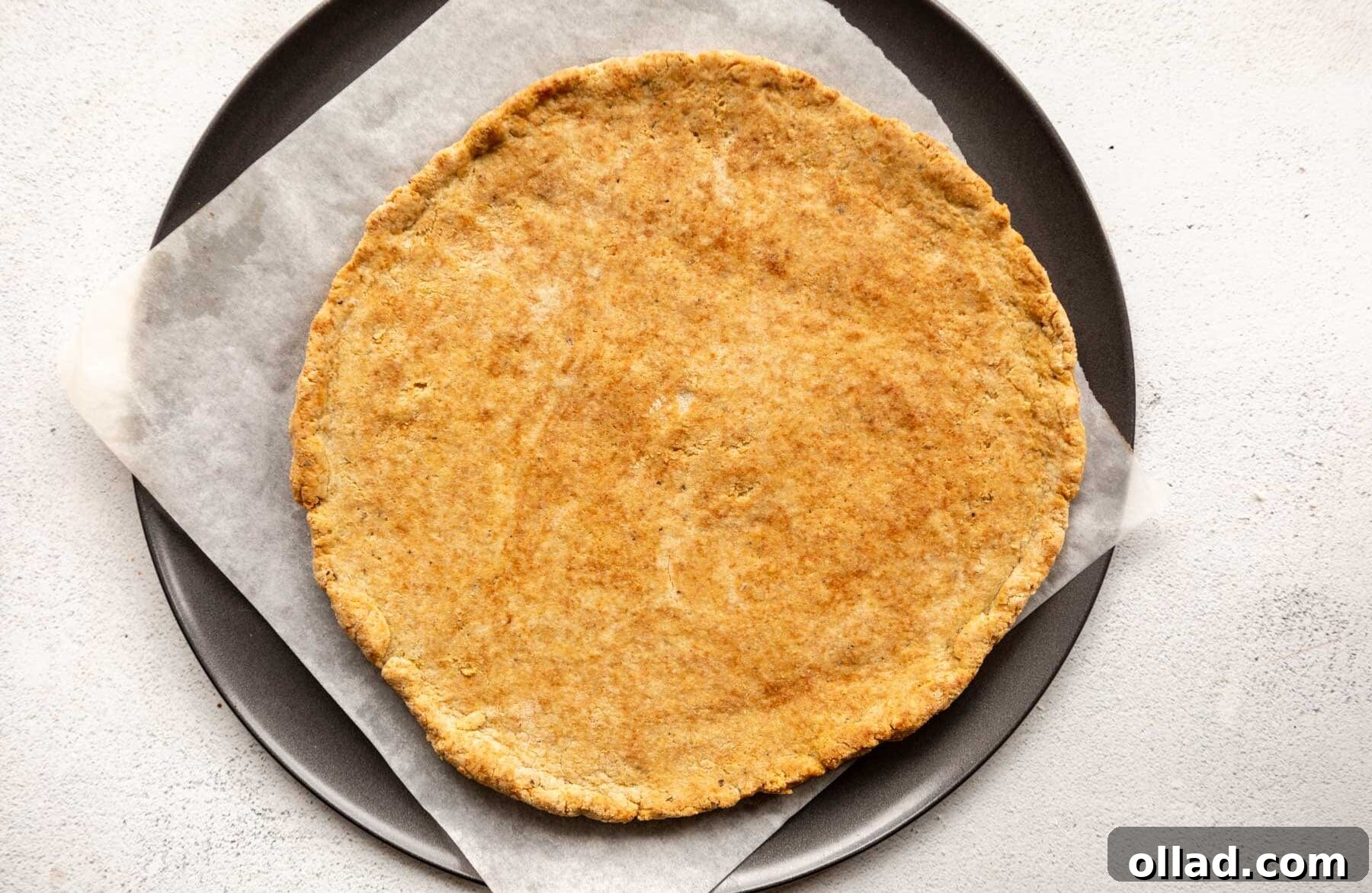 A pre-baked golden-brown almond flour pizza crust on a parchment-lined pizza pan, ready for toppings.