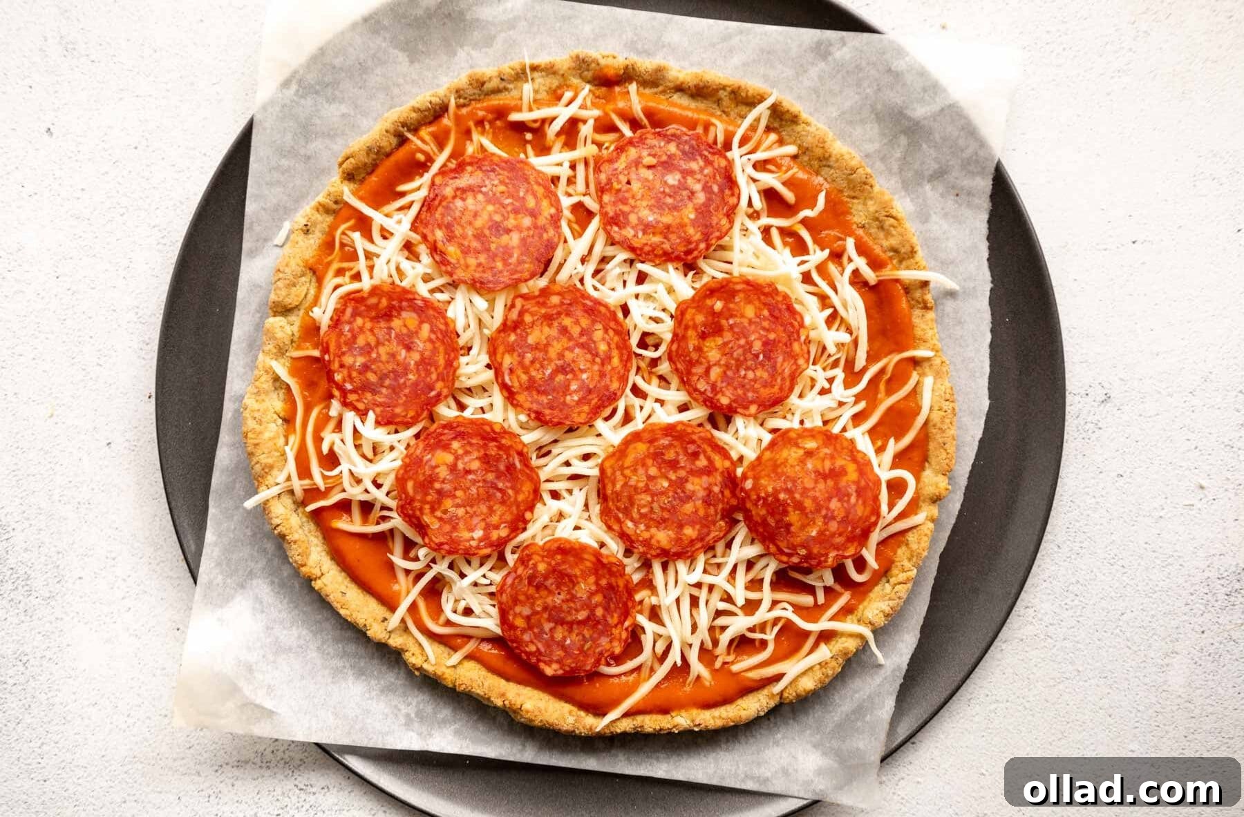 An almond flour pizza crust generously topped with sauce, cheese, and pepperoni, ready for its final bake.
