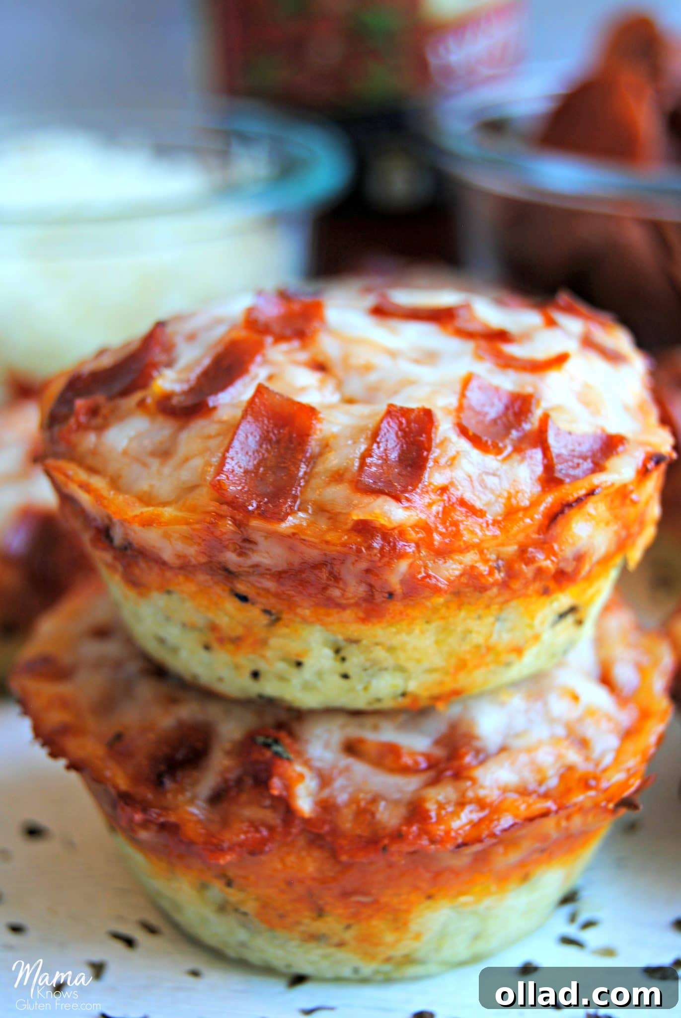 Two gluten-free deep dish pizza bites, perfectly golden, stacked on a plate with vibrant toppings visible in the background, hinting at their delicious potential.