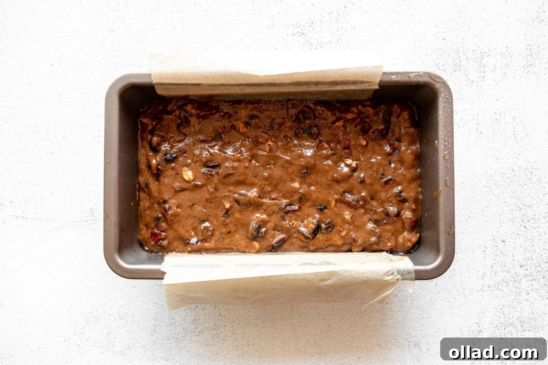 Deliciously Flourless Fruitcake 11 Gluten-free fruit cake batter spread evenly in a parchment-lined loaf pan, ready for baking.